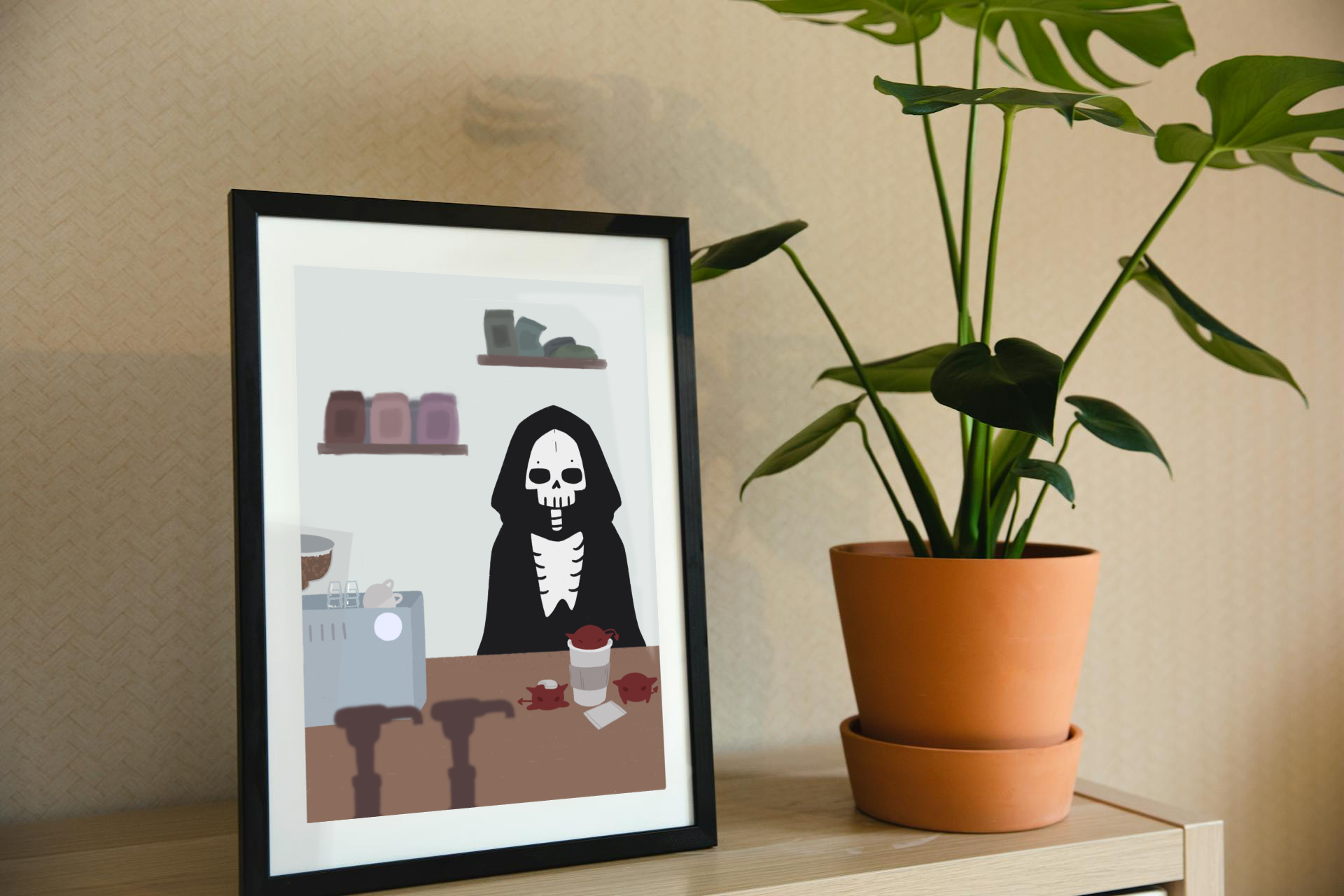 Framed art print on a shelf next to a house plant. The framed art print is of an illustration of a skeleton character standing behind a wooden counter with an espresso machine, a to-go coffee cup, and 3 red imps atop it.  In the forefront are the tops of syrup bottles, in the background are 2 shelves holding coffee bags on a light blue wall.