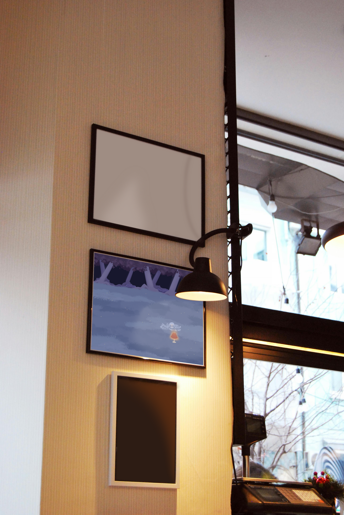 Framed art print hanging on a wall between blank frames next to a lit lamp and large window. The framed art print is of an illustration of a pile of bones in a field behind a lit lamp in the cool lighting of night. In the background is a dark forest covering the horizon.