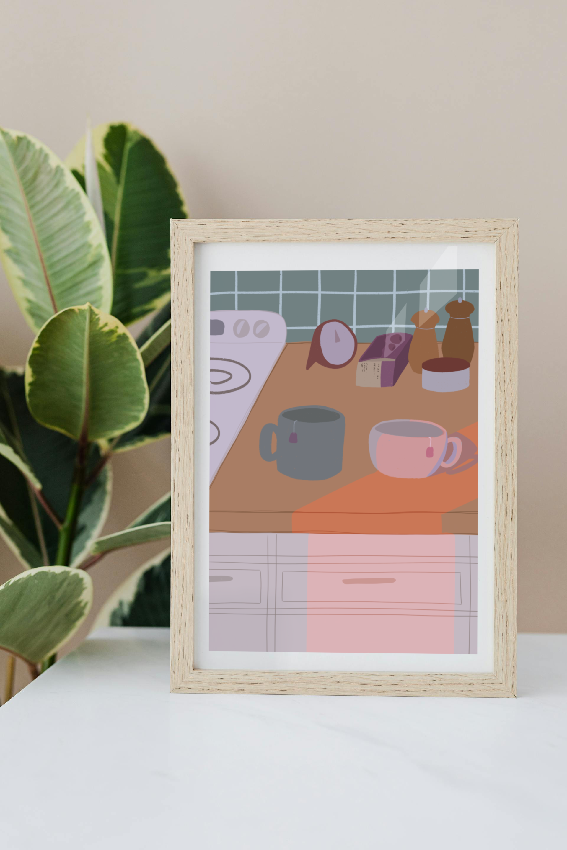 Framed art print on a white surface with a plant in the background of an illustration of a kitchen counter with two mugs holding tea bags in cool evening lighting. In the background are two pepper grinders, a tea box, a salt dish, and a timer. On the left is a white stovetop, white cabinet drawers at the bottom, and green tiles for the backsplash.