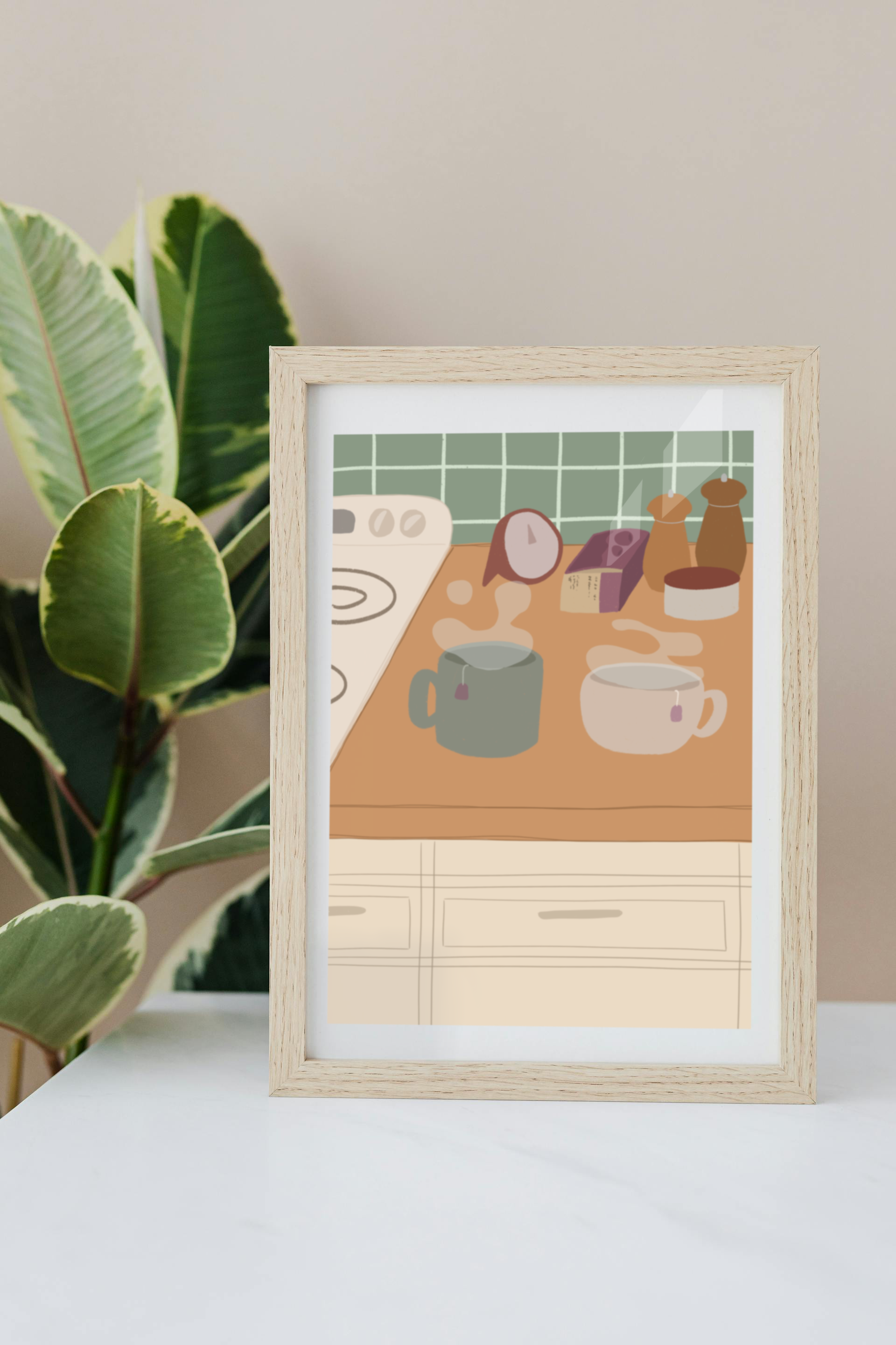 Framed art print on a white surface with a plant in the background of an illustration of a kitchen counter with two steaming mugs holding tea bags in morning lighting. In the background are two pepper grinders, a tea box, a salt dish, and a timer. On the left is a white stovetop, white cabinet drawers at the bottom, and green tiles for the backsplash.
