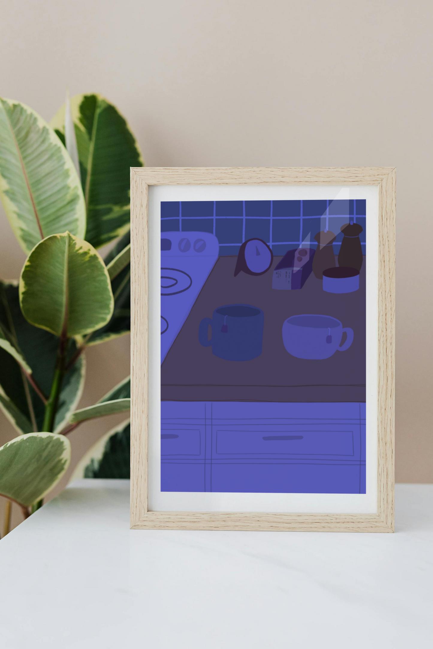 Framed art print on a white surface with a plant in the background of an illustration of a kitchen counter with two mugs holding tea bags in blue night lighting. In the background are two pepper grinders, a tea box, a salt dish, and a timer. On the left is a white stovetop, white cabinet drawers at the bottom, and green tiles for the backsplash.