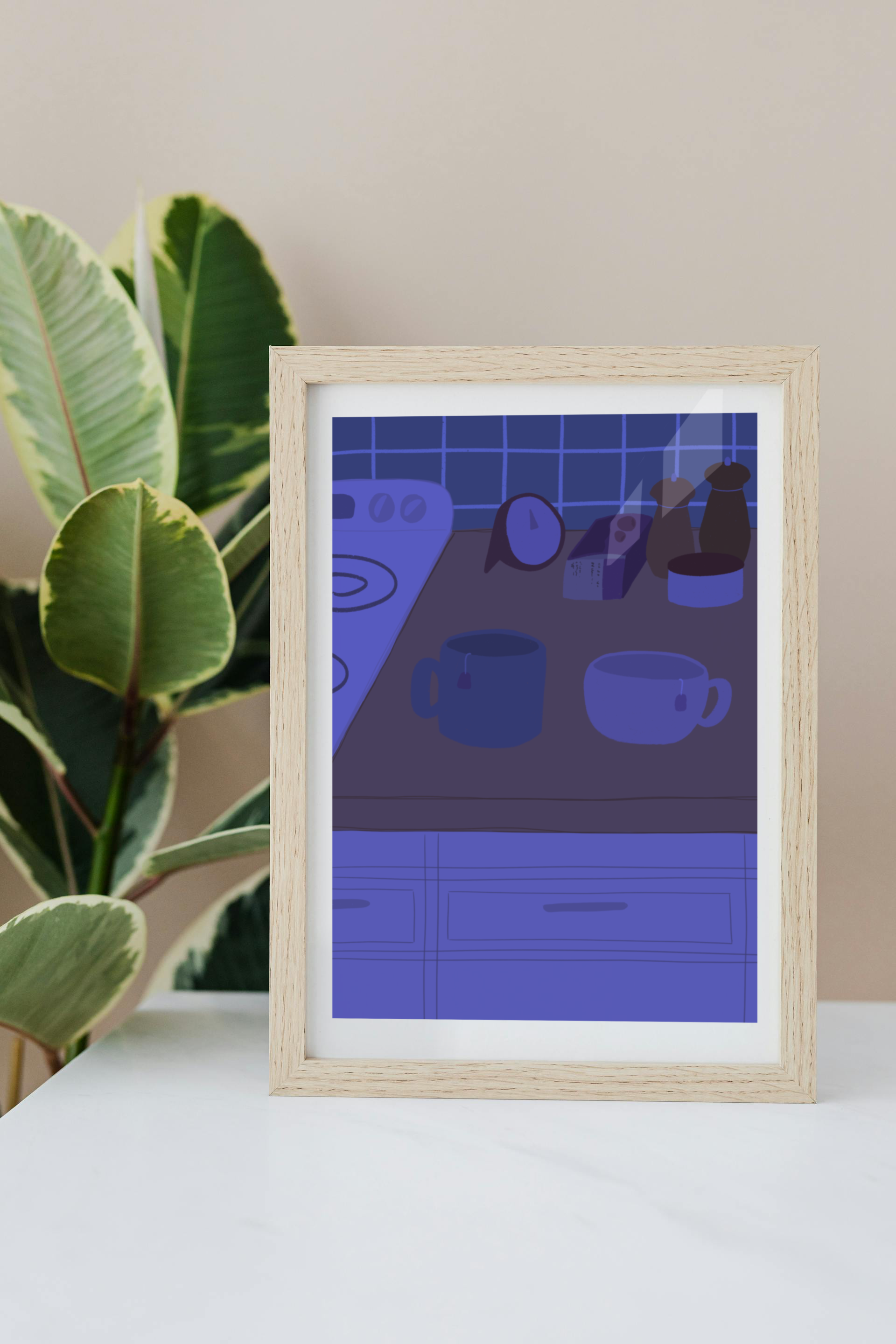 Framed art print on a white surface with a plant in the background of an illustration of a kitchen counter with two mugs holding tea bags in blue night lighting. In the background are two pepper grinders, a tea box, a salt dish, and a timer. On the left is a white stovetop, white cabinet drawers at the bottom, and green tiles for the backsplash.