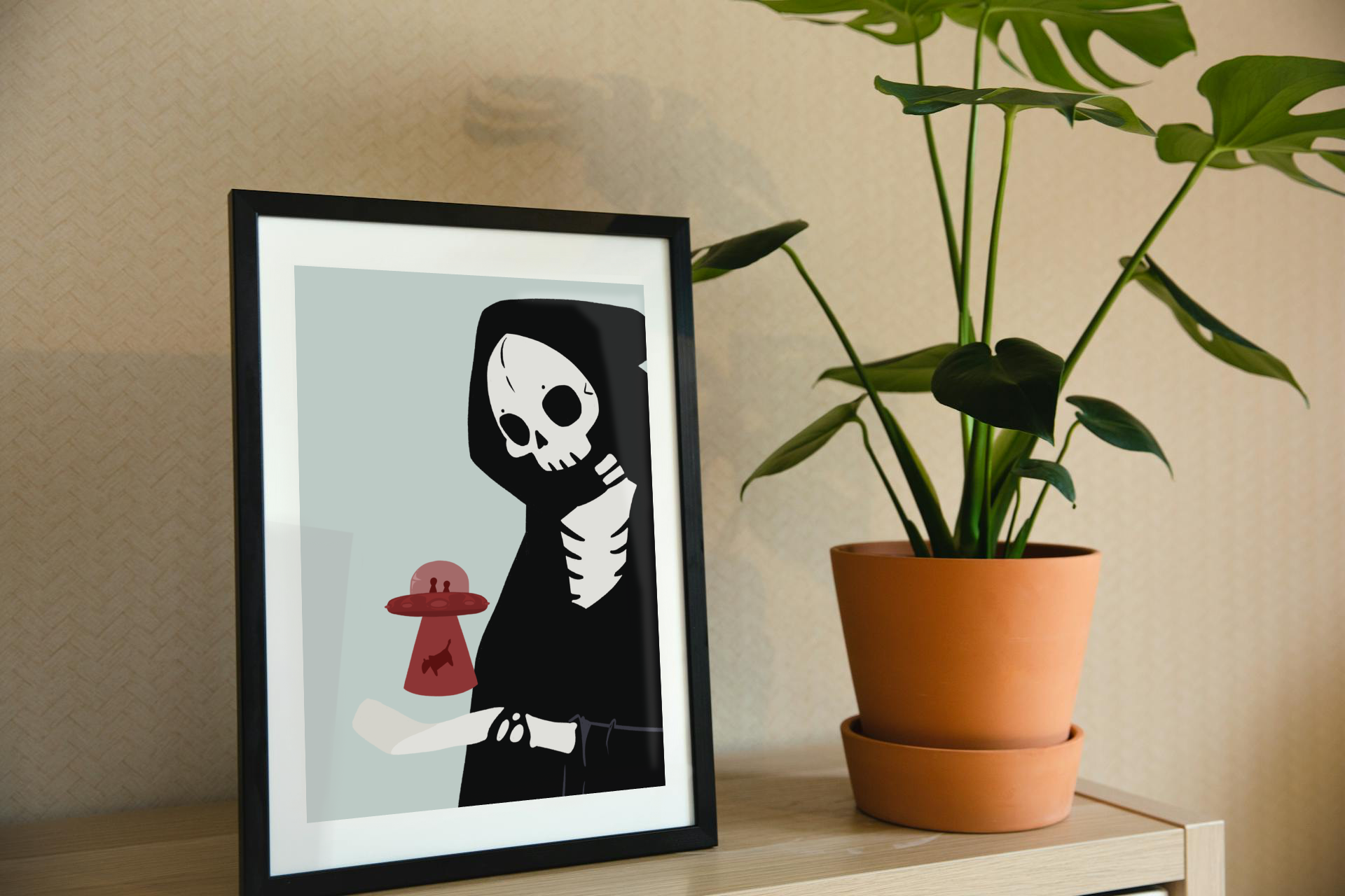 Framed art print on a shelf next to a house plant. The framed art print is of an illustration of a skeletal character with a red UFO abducting a cow hovering over its outreached hand in front of a light blue background.