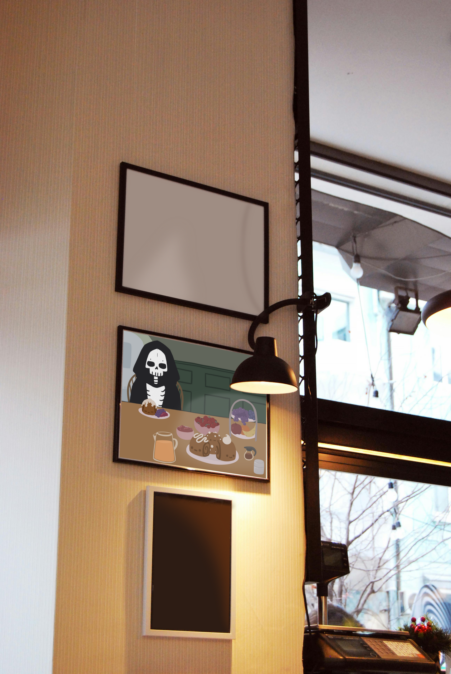 Framed art print hanging on a wall between blank frames next to a lit lamp and large window. The framed art print is of an illustration of a skeleton character sitting at a table with brunch foods, including orange juice, cinnamon rolls personified with faces and various frosting designs, various fruits, a bowl of cherry tomatoes, syrup, jam, and powdered sugar. The background is of a green wall and hallway.