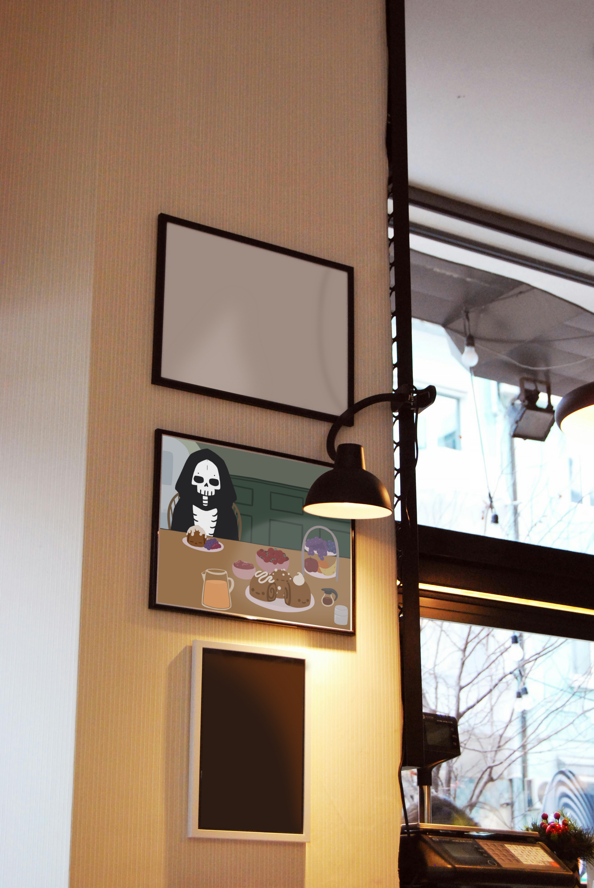 Framed art print hanging on a wall between blank frames next to a lit lamp and large window. The framed art print is of an illustration of a skeleton character sitting at a table with brunch foods, including orange juice, cinnamon rolls personified with faces and various frosting designs, various fruits, a bowl of cherry tomatoes, syrup, jam, and powdered sugar. The background is of a green wall and hallway.