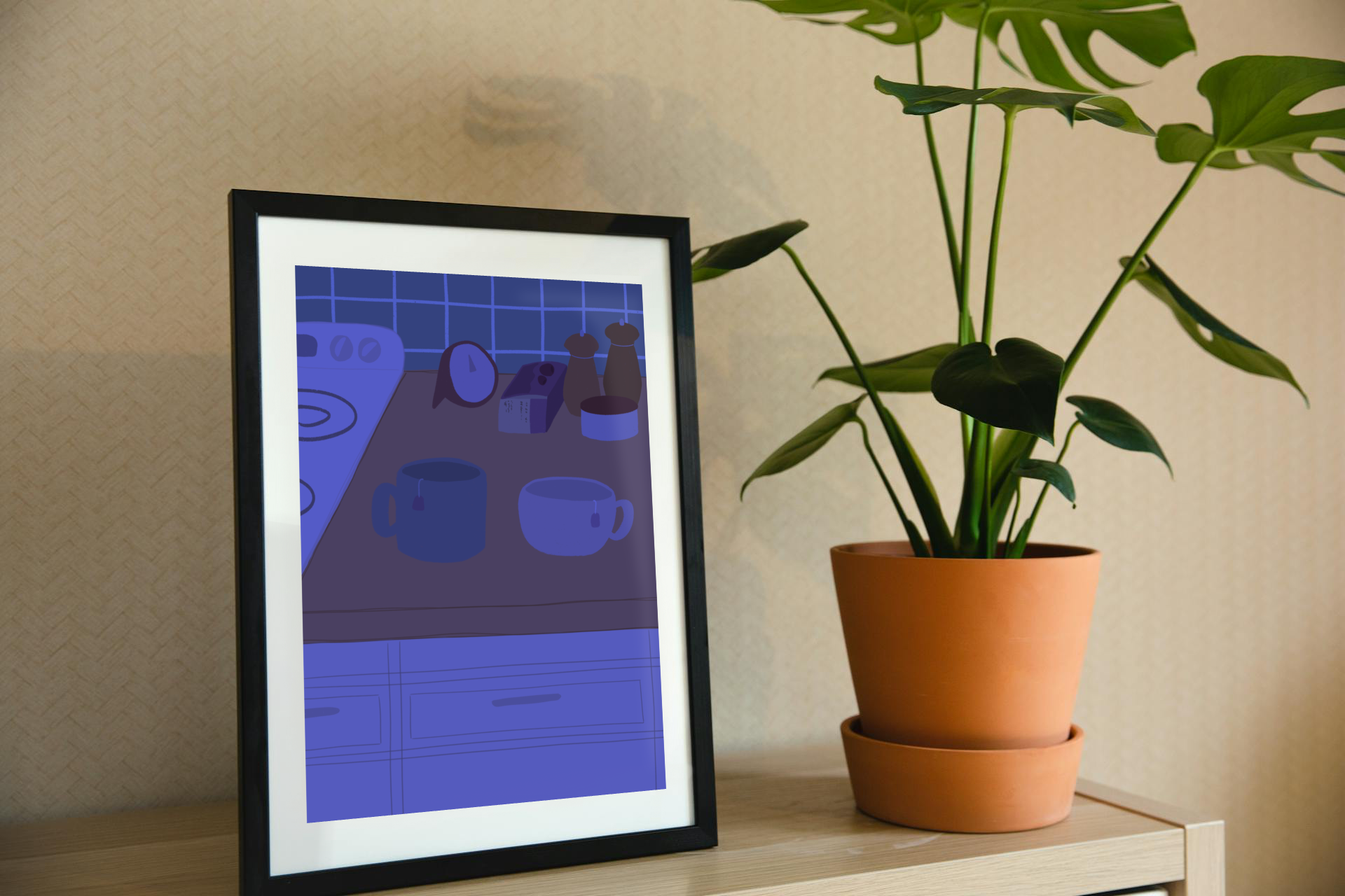 Framed art print on a shelf next to a house plant. The framed art print is of an illustration of a kitchen counter with two mugs holding tea bags in blue night lighting. In the background are two pepper grinders, a tea box, a salt dish, and a timer. On the left is a white stovetop, white cabinet drawers at the bottom, and green tiles for the backsplash.