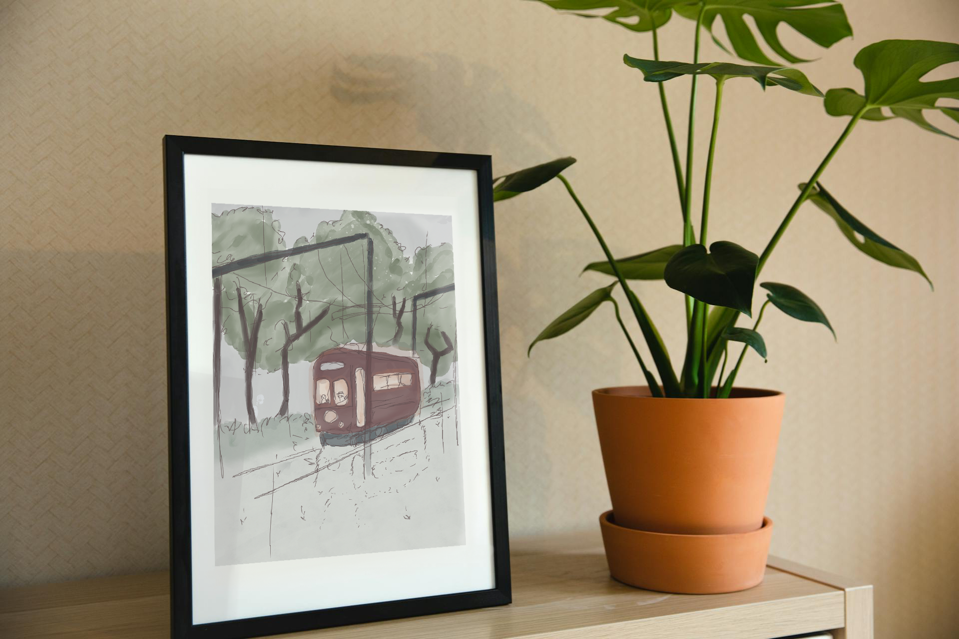 Framed art print on a shelf next to a house plant. The framed art print is of an illustration of a watercolor-style tram in a forest with trees, a cloudy sky, and light rain. A beaver and raccoon drive the tram, while a skeleton hidden in the trees watches as it passes by.