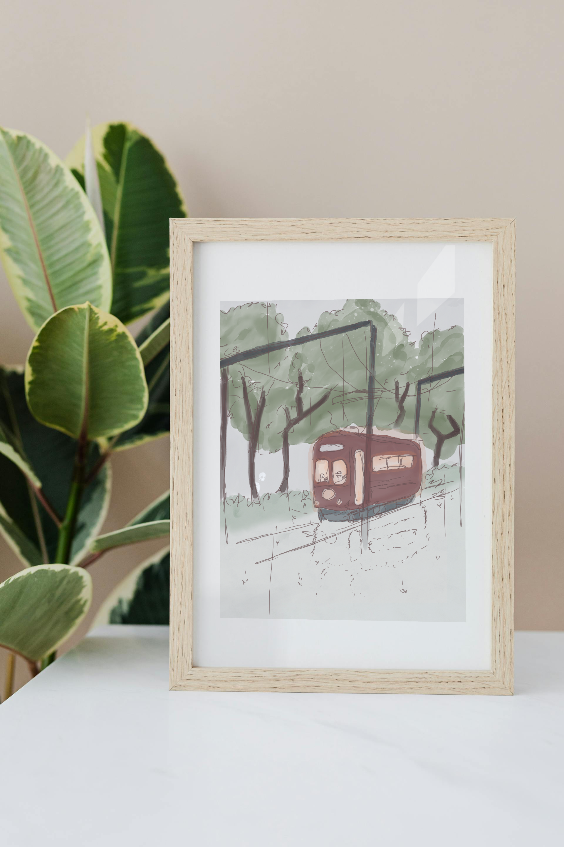 Framed art print on a white surface with a plant in the background of an illustration of a watercolor-style tram in a forest with trees, a cloudy sky, and light rain. A beaver and raccoon drive the tram, while a skeleton hidden in the trees watches as it passes by.